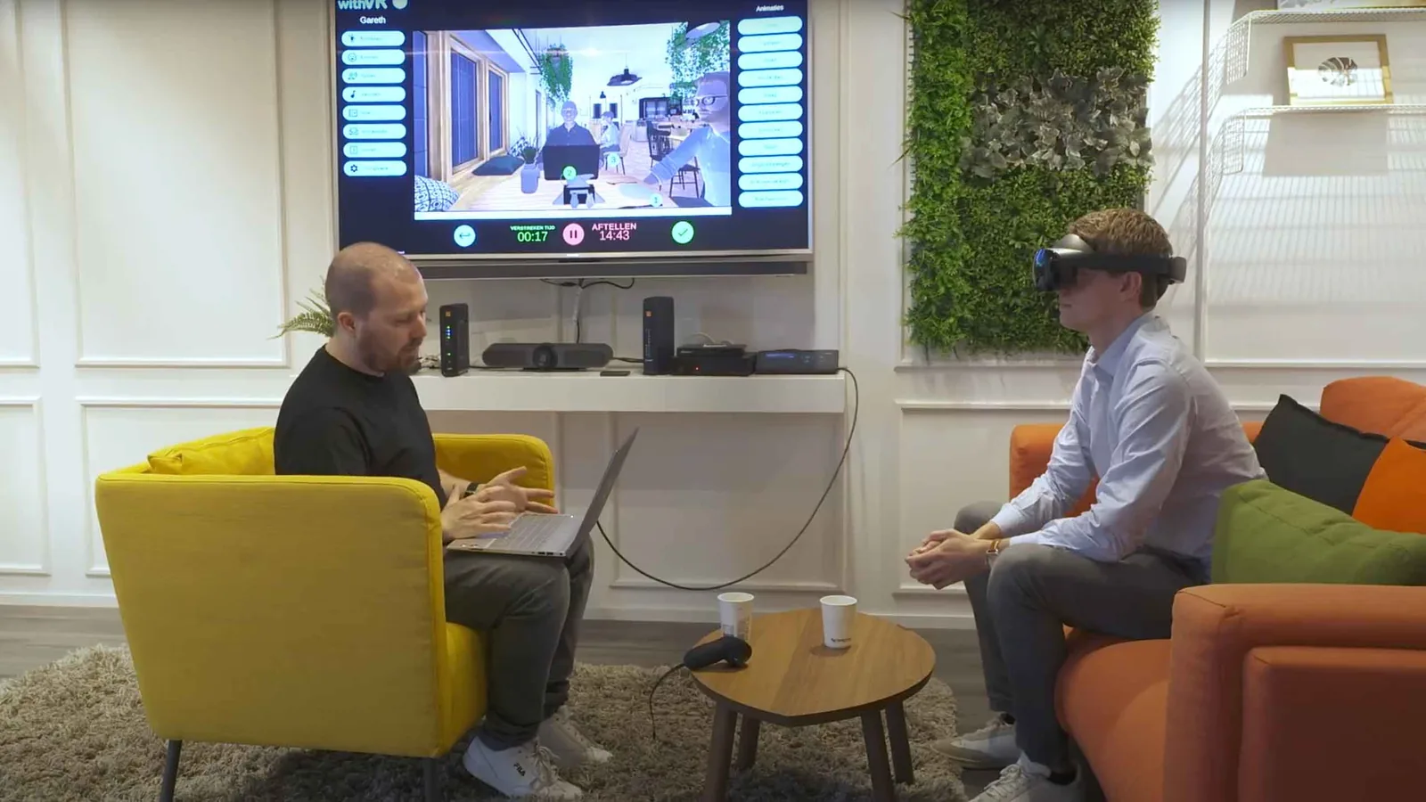 A young person wearing a VR headset while a therapist controls the virtual speaking situation from a laptop in the background.