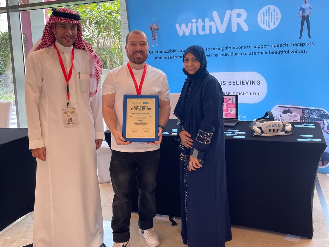 Gareth Walkom يتسلّم شهادة تقدير بعد محاضرته في المملكة العربية السعودية، إلى جانب لافتة withVR